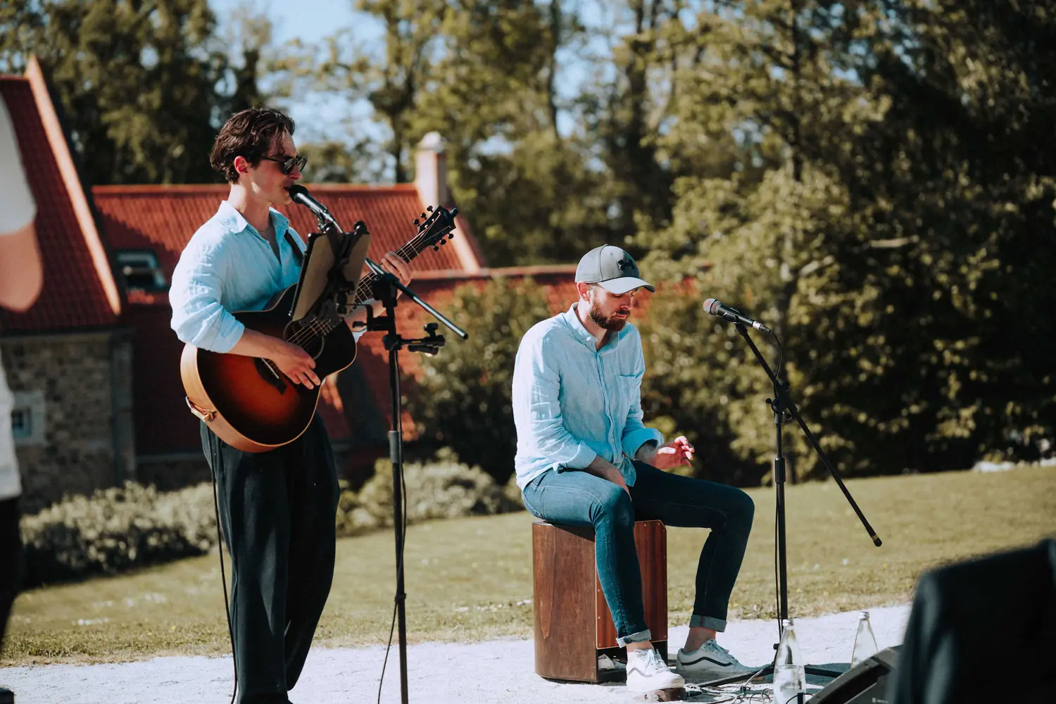 Carl à la guitare et au chant, accompagné au cajon, en plein air
